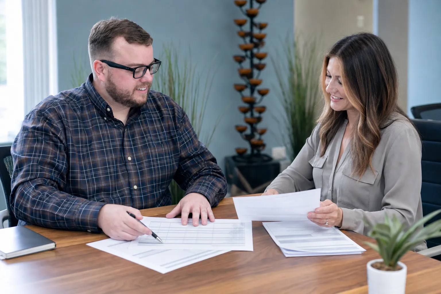 Two people sitting at a table review documents together; one person points at a paper while the other holds a sheet and smiles.